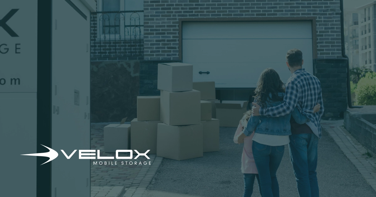 A Velox portable storage container parked on a residential driveway next to an open garage during a weekend decluttering and cleanout project.