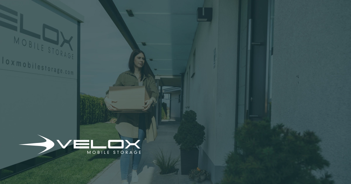 A female college student carries a packing box near a Velox Mobile Storage container during semester move-out.