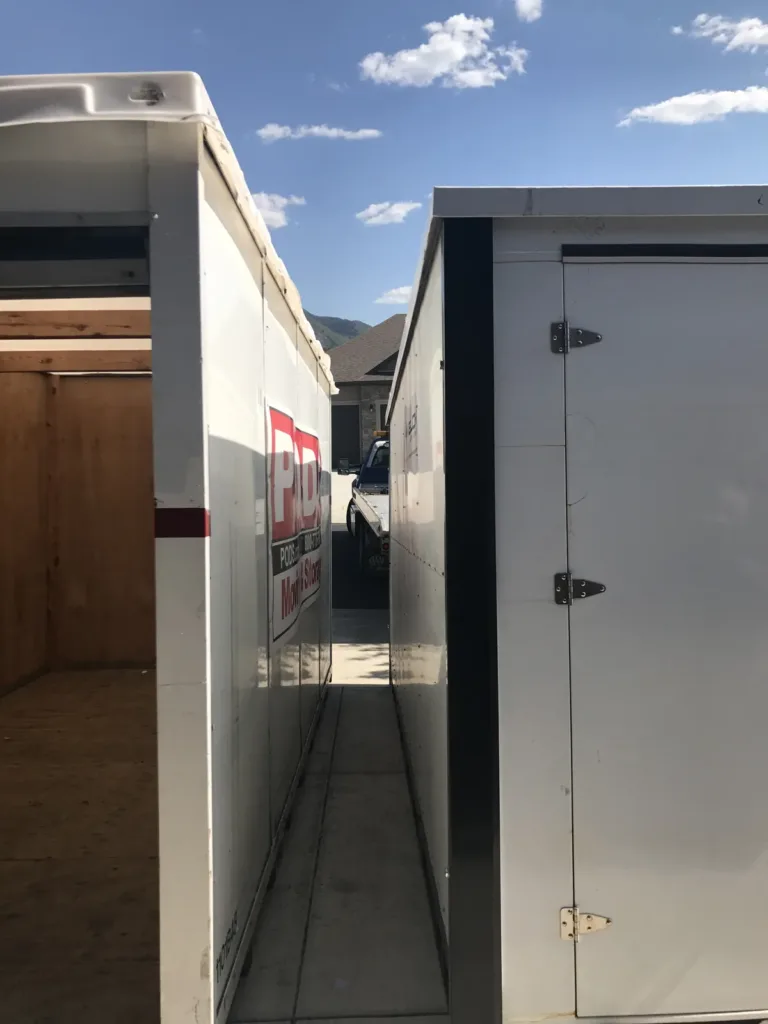 An open storage container with wood-lined walls and floor on the left, next to a white Velox container with steel door hinges on the right