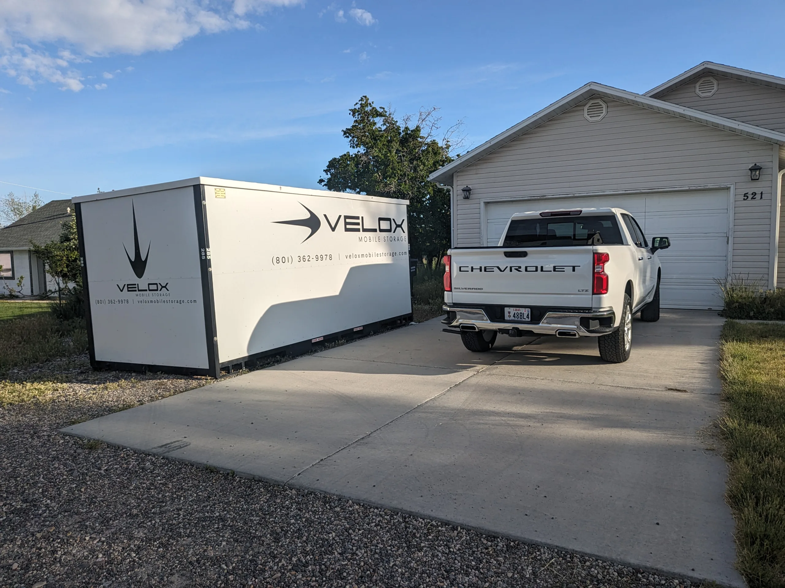 A Velox Mobile Storage container parked in a driveway beside a garage