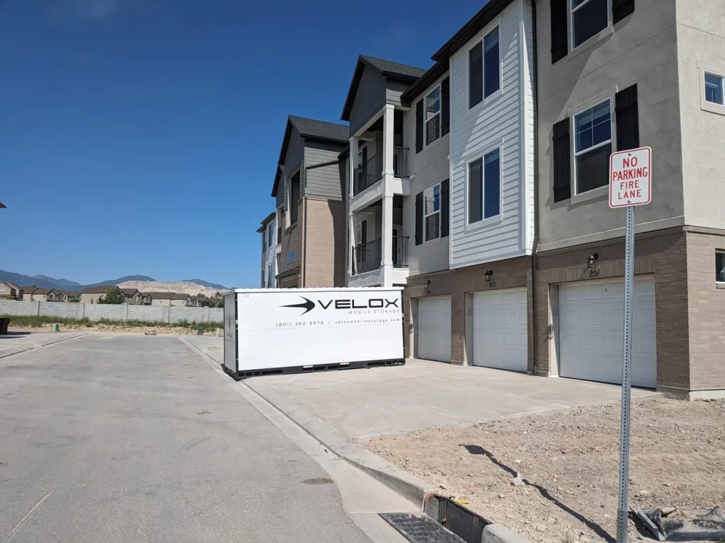 A Velox Mobile Storage container set on a new-construction driveway beside townhome garages in Riverton, Utah
