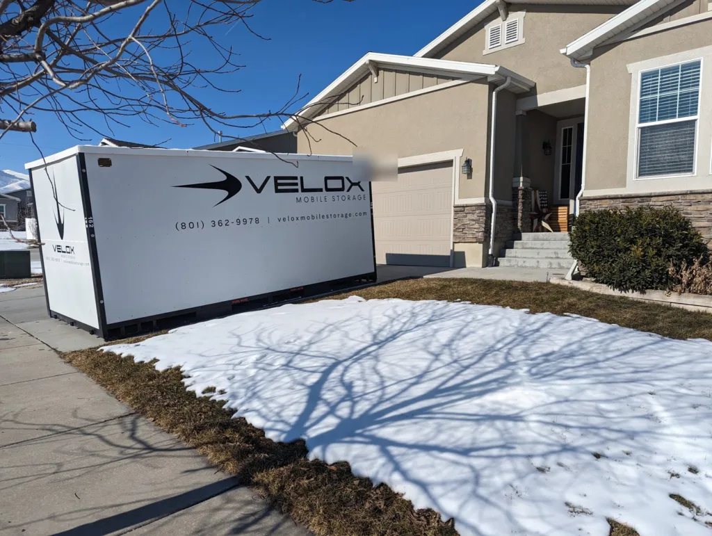 A Velox Mobile Storage container on a driveway beside a home in West Jordan, Utah, with snow on the lawn