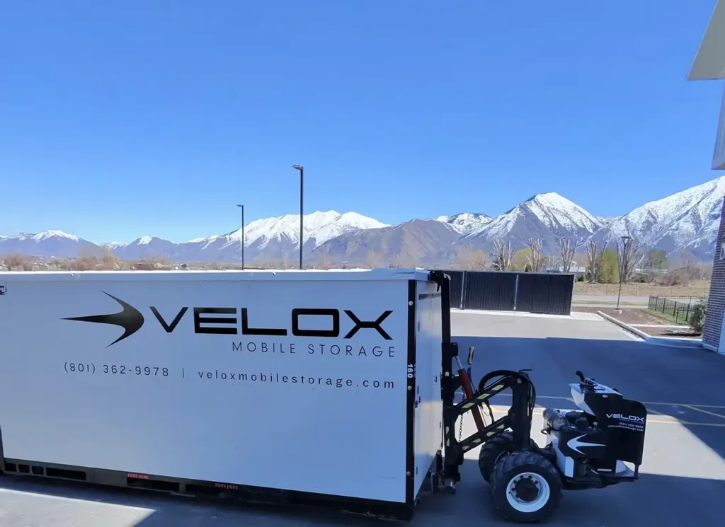 Velox Mule setting a portable storage container in an apartment parking lot in Payson, Utah, with snowy mountains behind