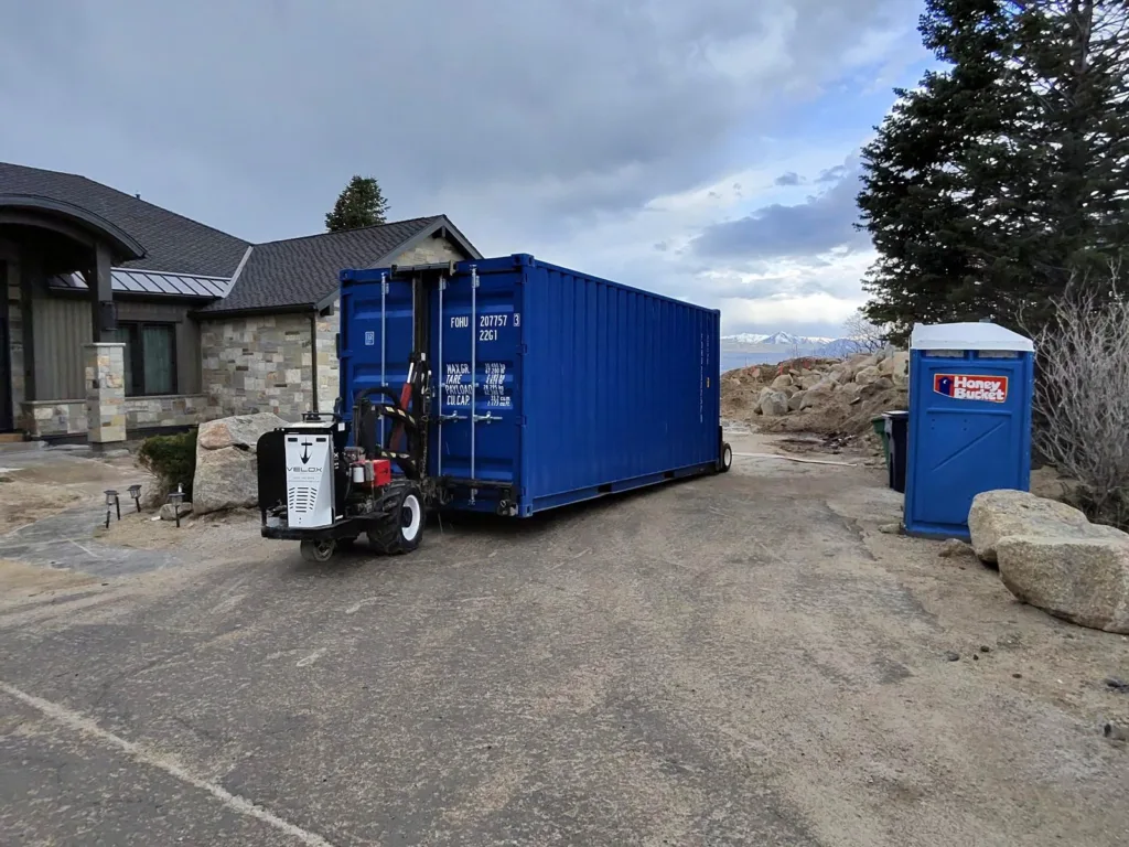 The Velox Mule machine setting a blue shipping container on a hillside lot on the Sandy, Utah east bench